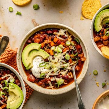 Three bean chili with cheddar, sour cream, avocado on top and spoon.