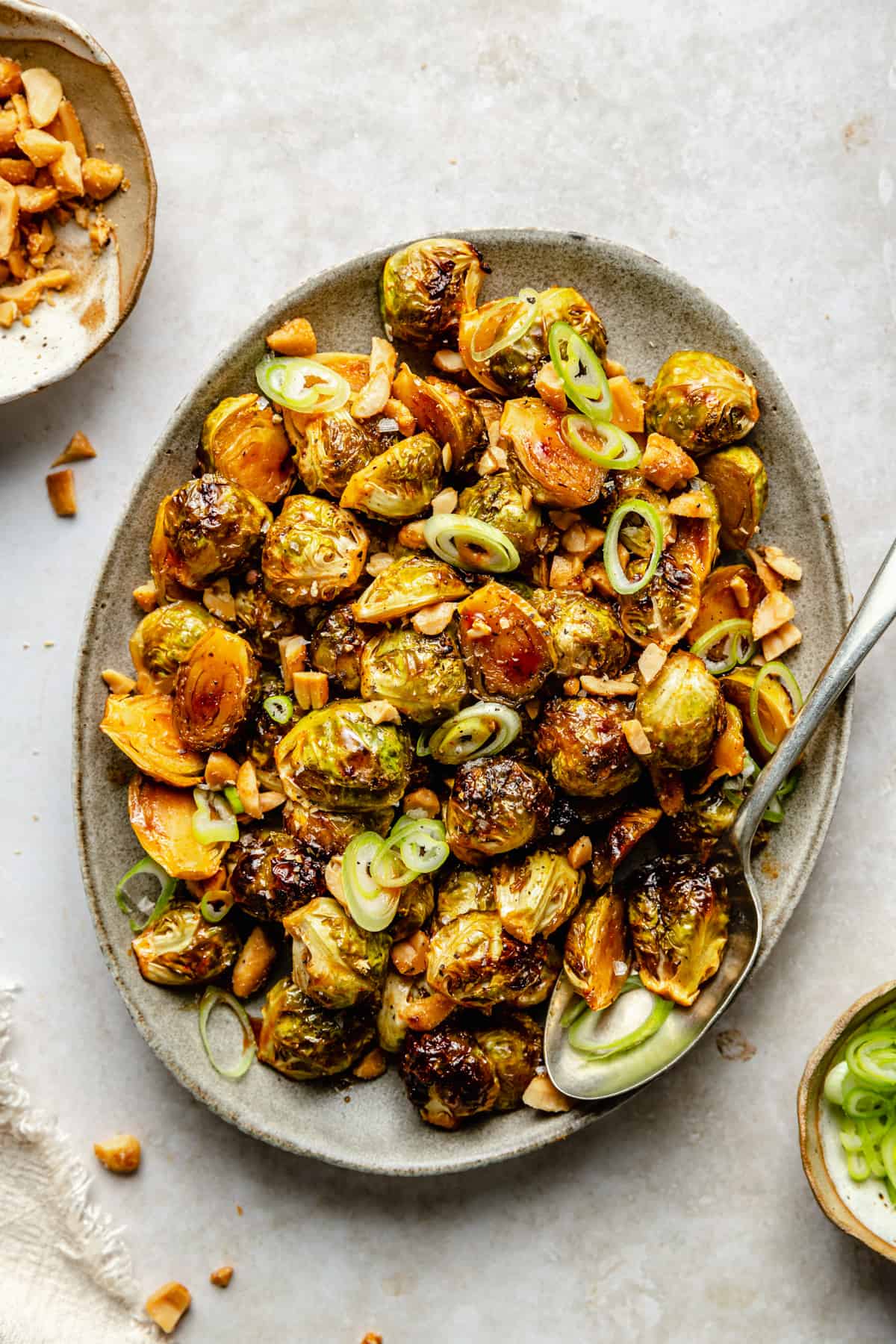 A platter of honey sriracha brussels sprouts topped with nuts and green onion with a spoon.