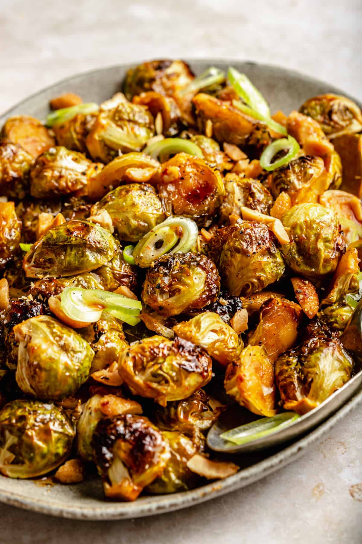 Close up of caramelized brussels sprouts glazed with honey and sriracha on a platter with a spoon.