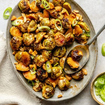 Honey sriracha brussels sprouts on a platter with a spoon serving them up.
