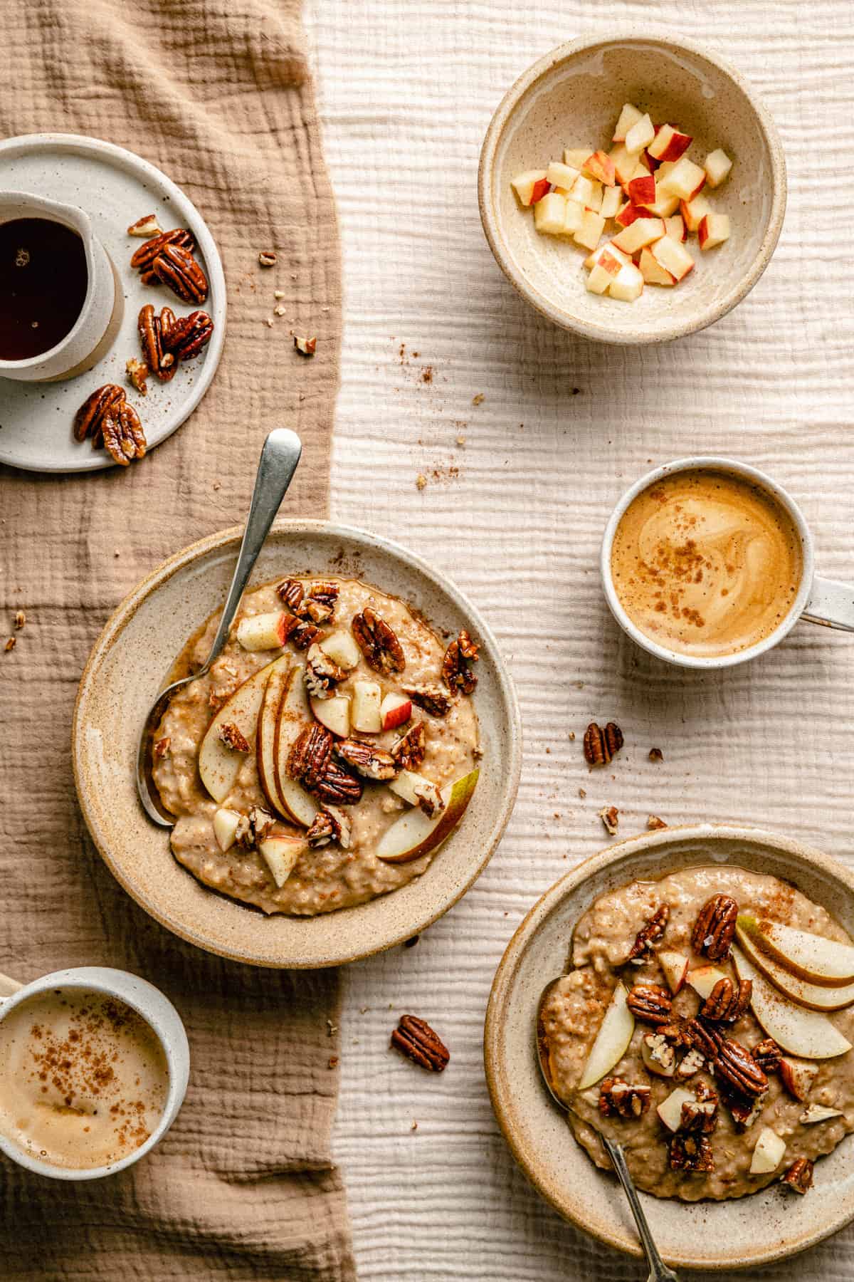 Two bowls of maple brown sugar oatmeal topped with nuts and fruit with coffee and more syrup in a jug nearby.
