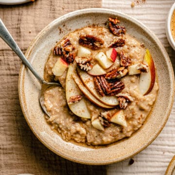 Maple brown sugar oatmeal served in a bowl with a spoon topped with nuts and fruit.