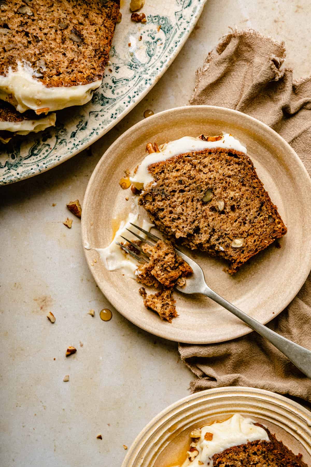 A slice of banana pecan bread served on a plater with a fork taking a chunk. 