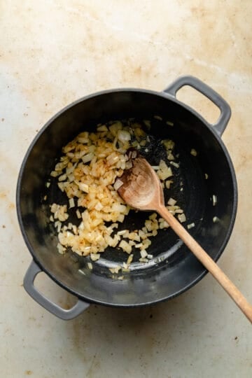 Sweating down the diced onion in a large cast iron pan with a wooden spoon.