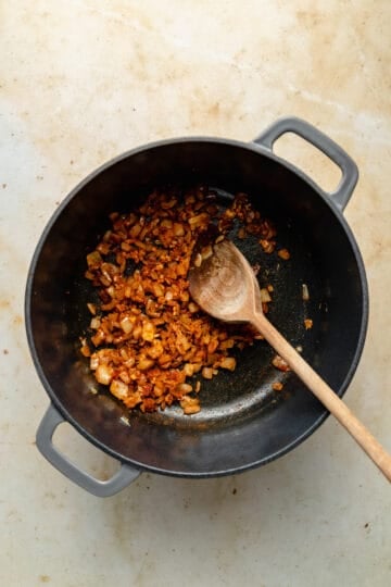 Spices and garlic stirred together in a cast iron dutch oven with wooden spoon.