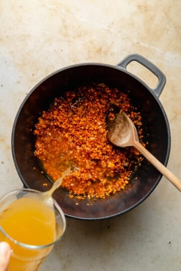 Stock being poured into a pan with a wooden spoon.