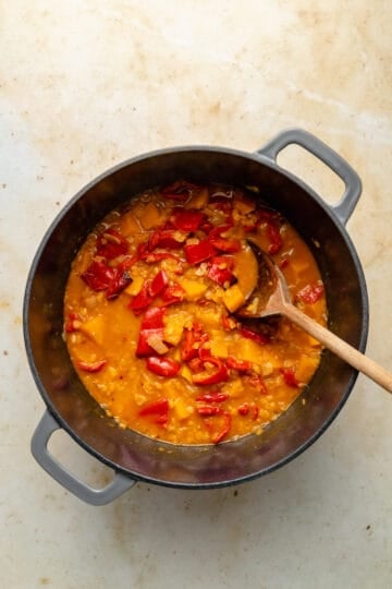 Pre blended butternut squash and red pepper soup in a pan with a spoon.