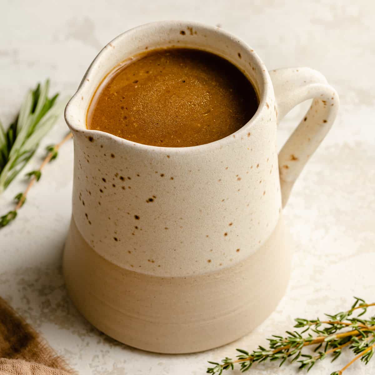 Roast chicken gravy served in a jug with herbs and napkin to the side. 