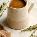 A jug of chicken gravy with herbs and a napkin around.