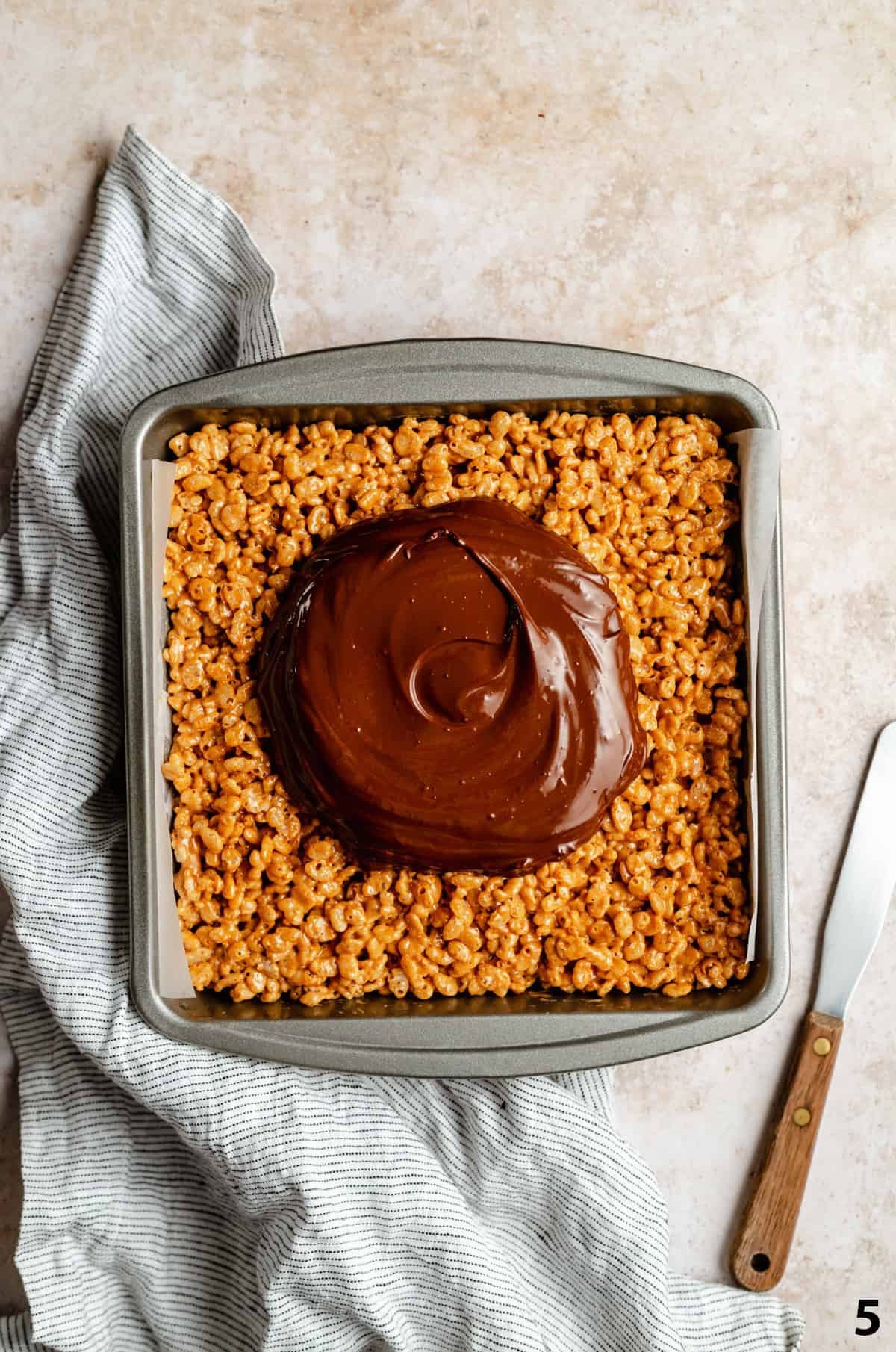 Rice krispie treats in a baking tin with melted chocolate mix on top being spread out.