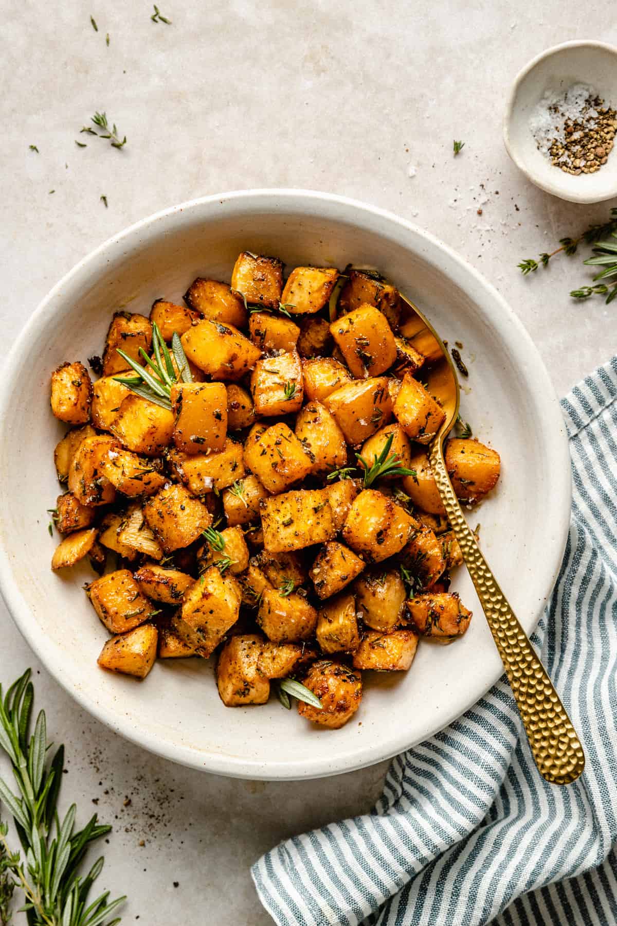 A bowl of glistening roasted swede in a bowl with a napkin and a dish of seasoning to the side.