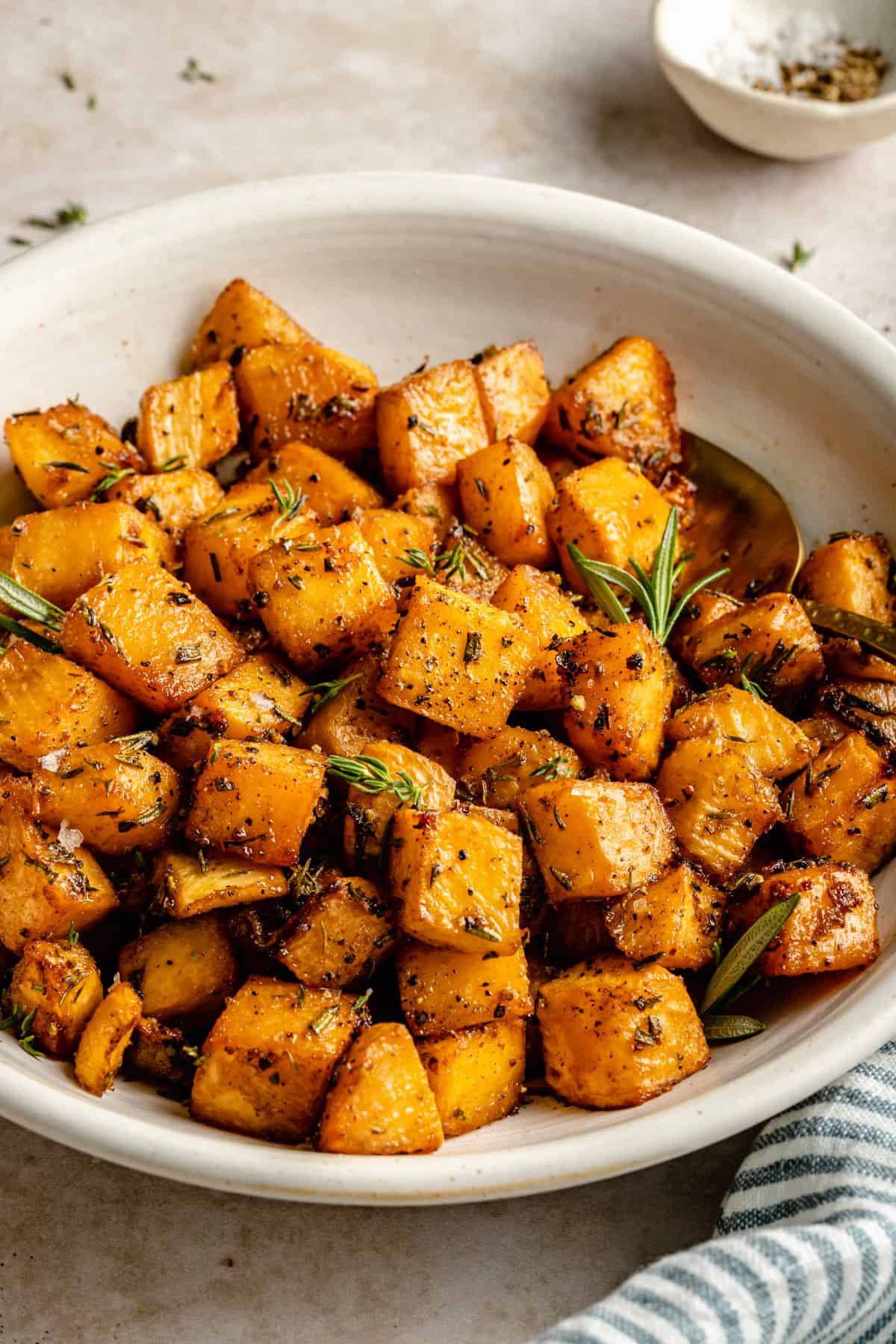Roasted swede (rutabaga) cubes coated in herbs in a bowl with a spoon with a dish in the background.