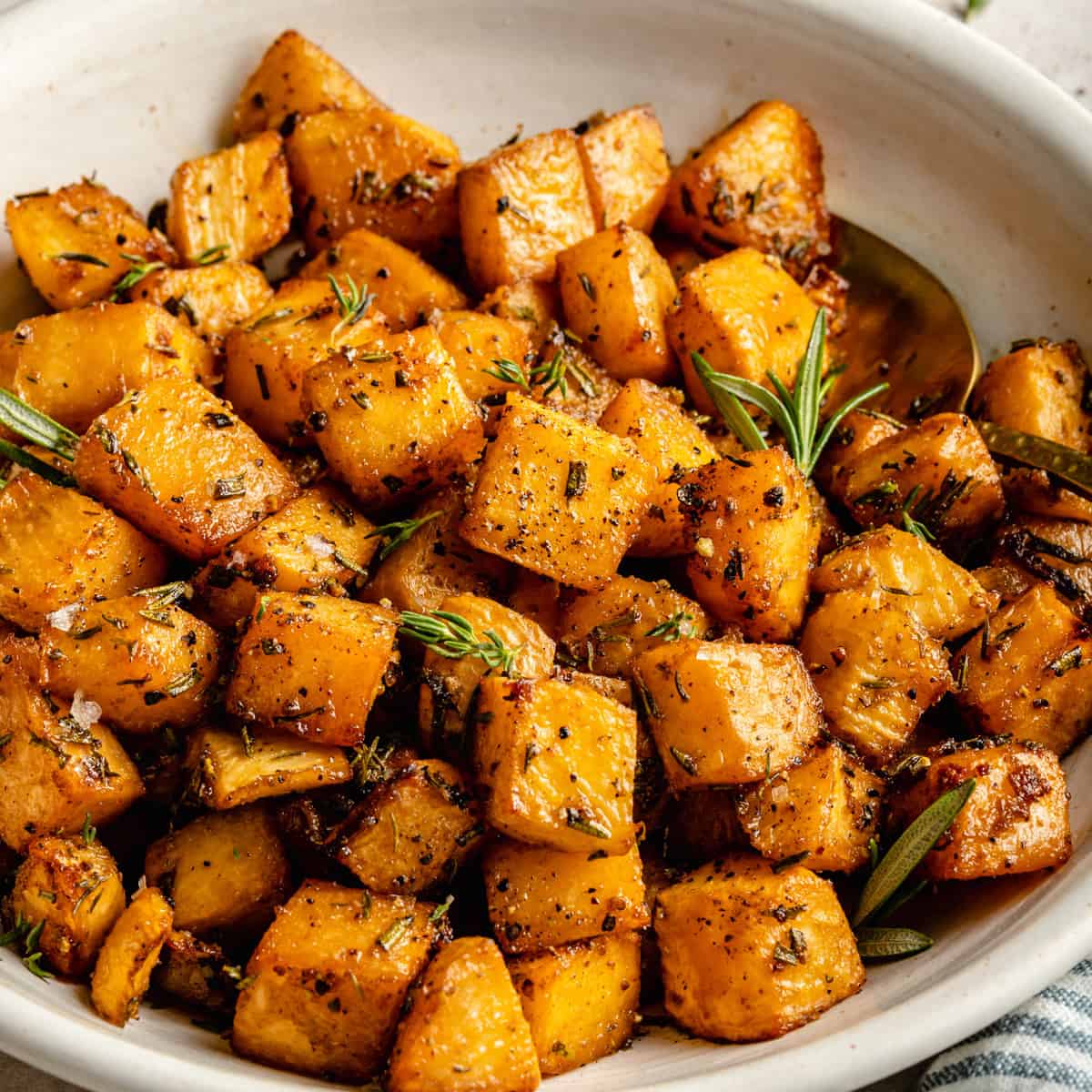 Roasted swede (rutabaga) cubes in a bowl with a spoon with a dish in the background.