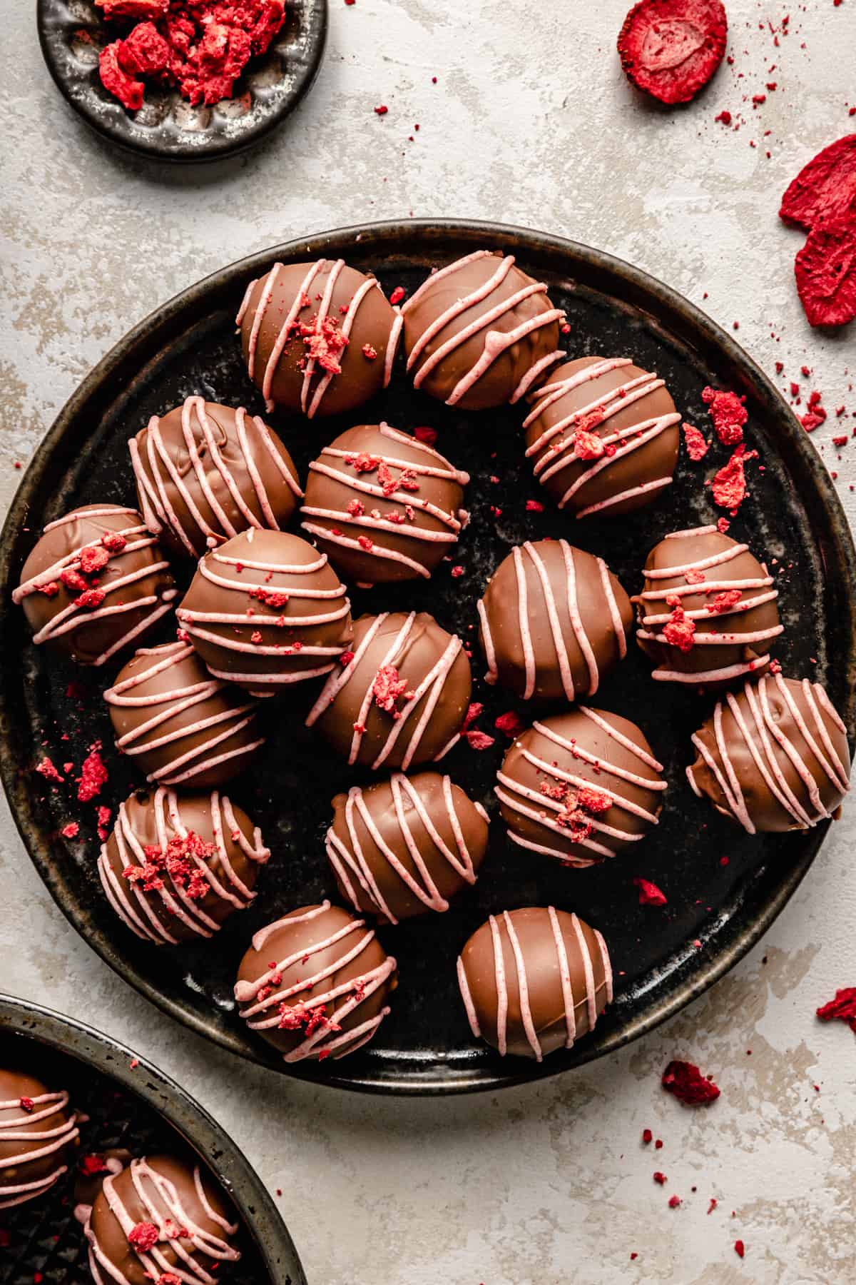 An overhead of strawberry truffles on a dark plate with freeze dried strawberries around.