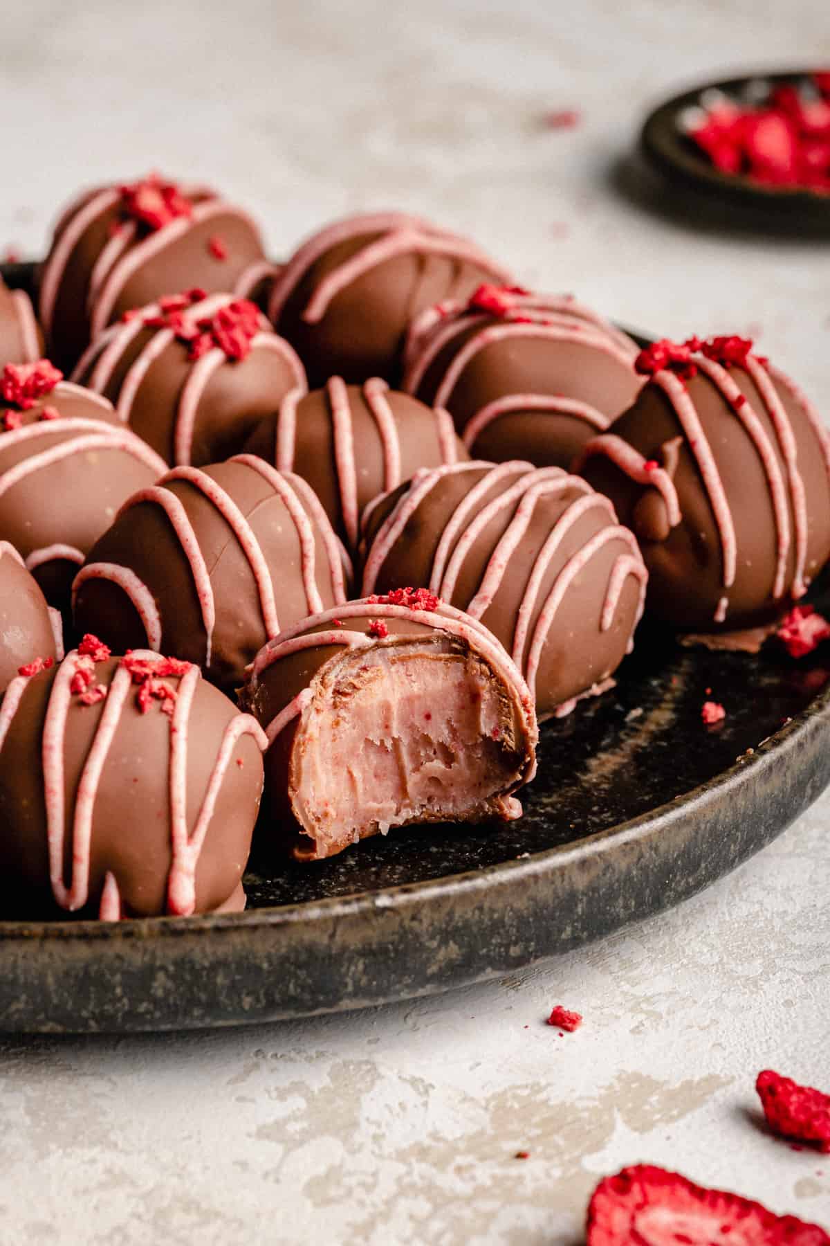 Strawberry truffles on a plate with one with a bite taken out showing the pink centre.