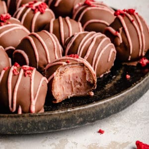 Strawberry truffles on a plate, one with a bite taken out showing the inside.
