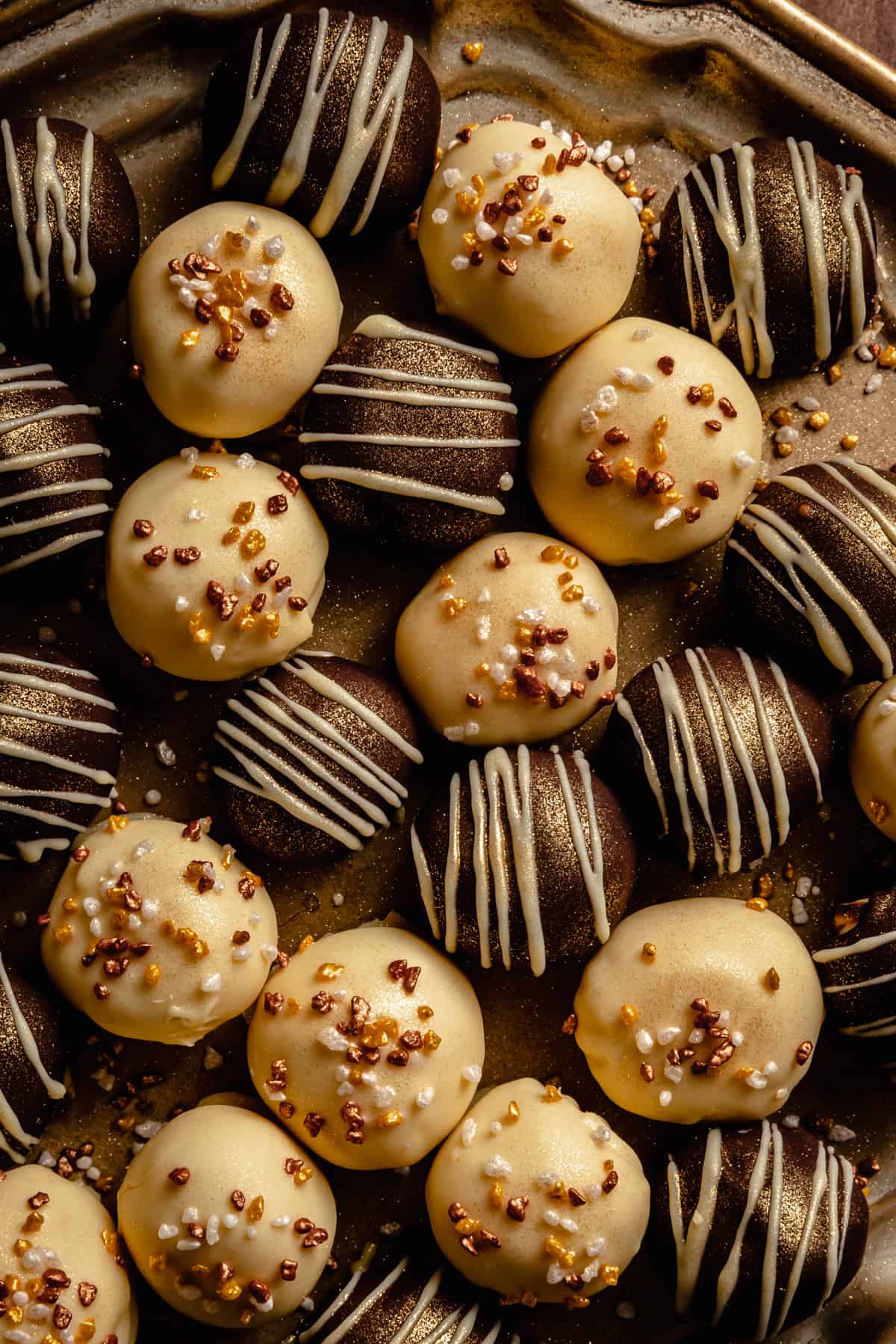 An array of white chocolate truffles on a gold platter decorated with sprinkles and gold glitter.