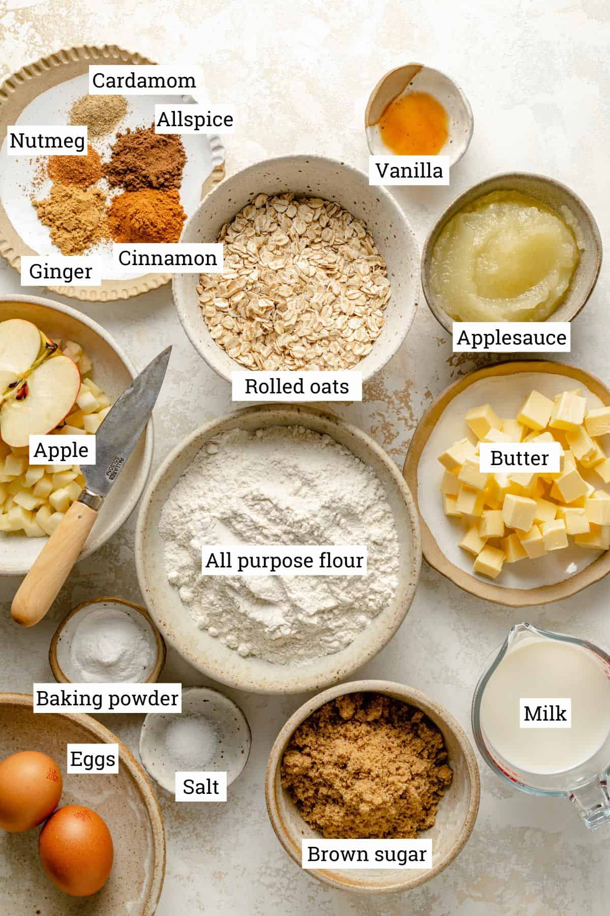 Ingredients for apple oatmeal muffins in various bowls on a work surface.