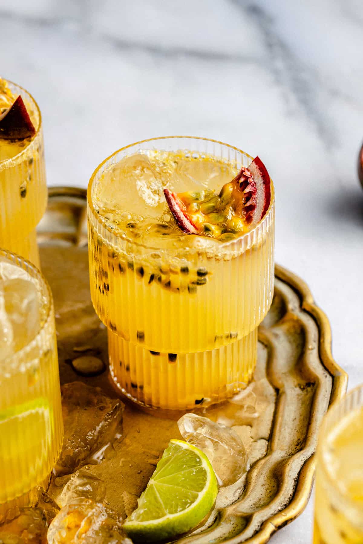 Glasses of passionfruit mocktail on a gold tray with ice and lime wedges.