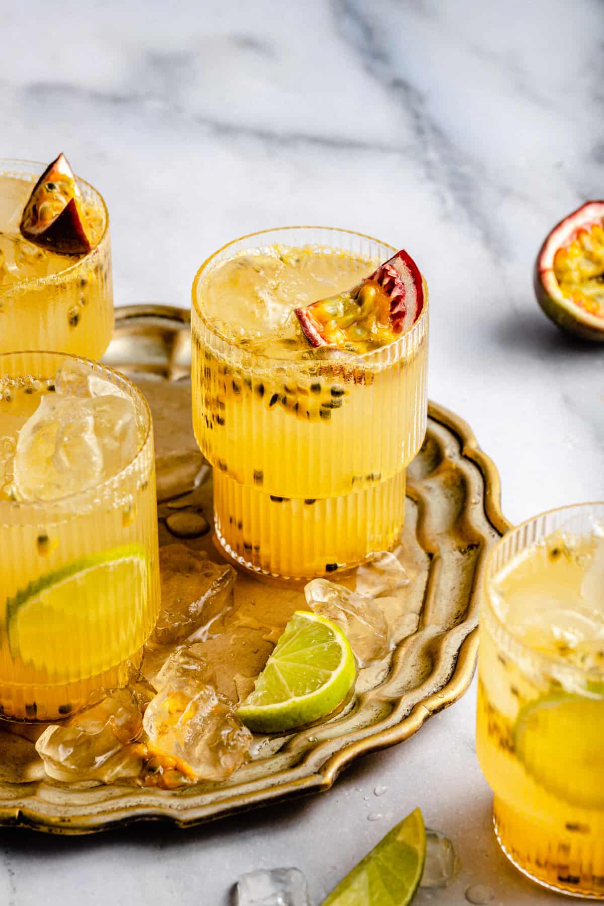 Multiple glasses of passionfruit mocktail on a gold tray with passionfruit and ice in the glasses.