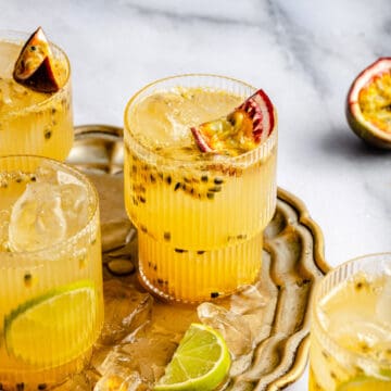 passionfruit mocktail in glasses on a gold tray with passionfruit, lime slices and ice around.