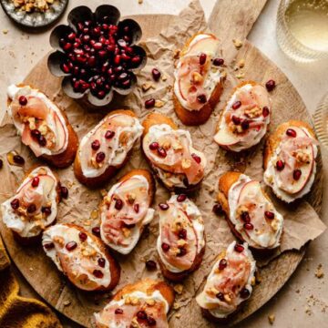 Ricotta Crostini served on a wooden platter with pomegranate arils to the side with a napkin.