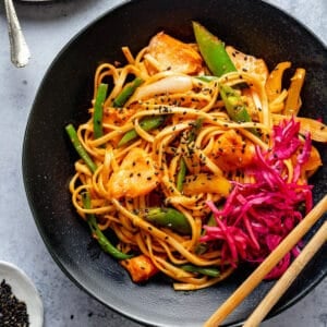 Gochujang noodles with salmon and a quick pickle served in a black bowl with chopsticks to the side.