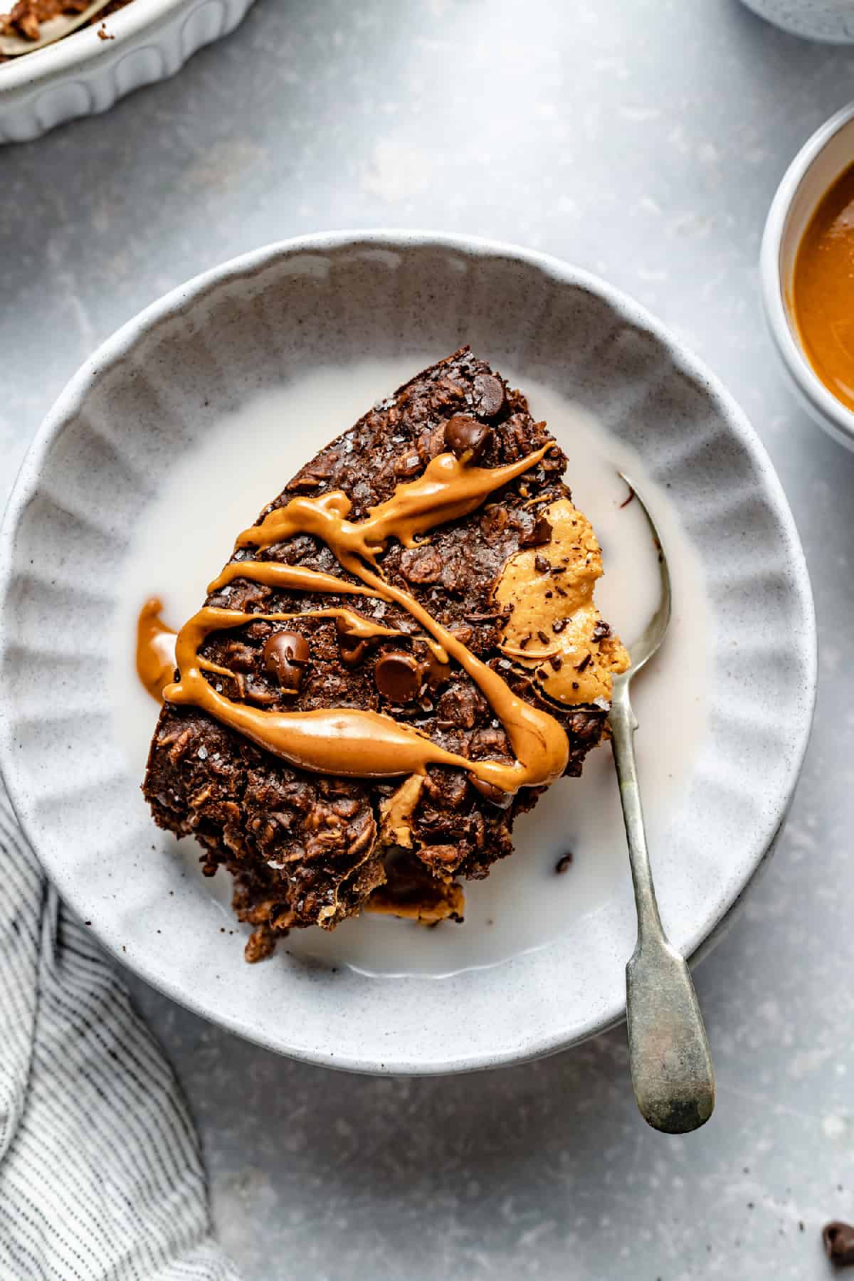 A bowl with a portion of peanut butter baked oatmeal served up with peanut butter and milk with a spoon.