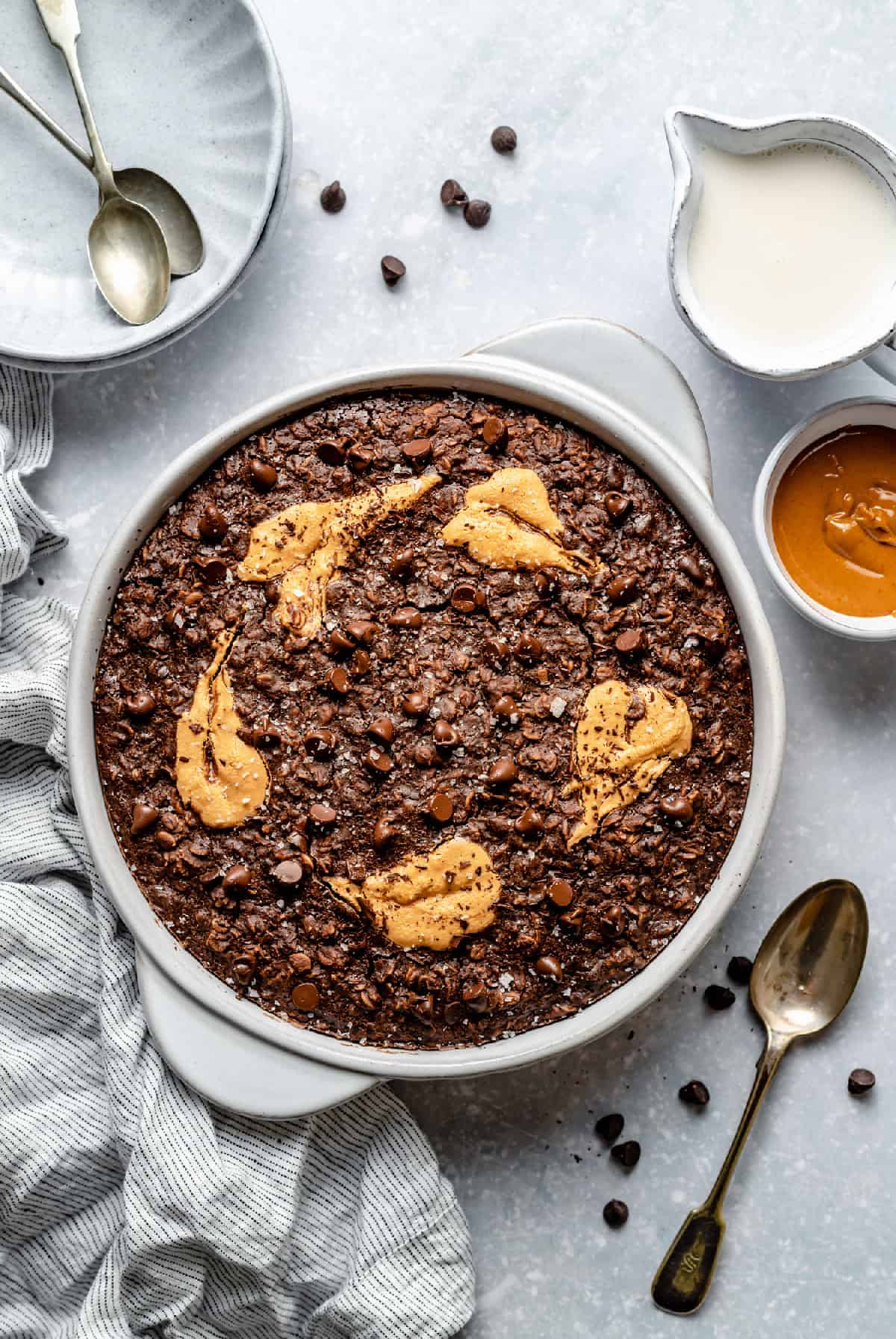 The baked chocolate peanut butter baked oatmeal in a dish with a spoon and bowls nearby.