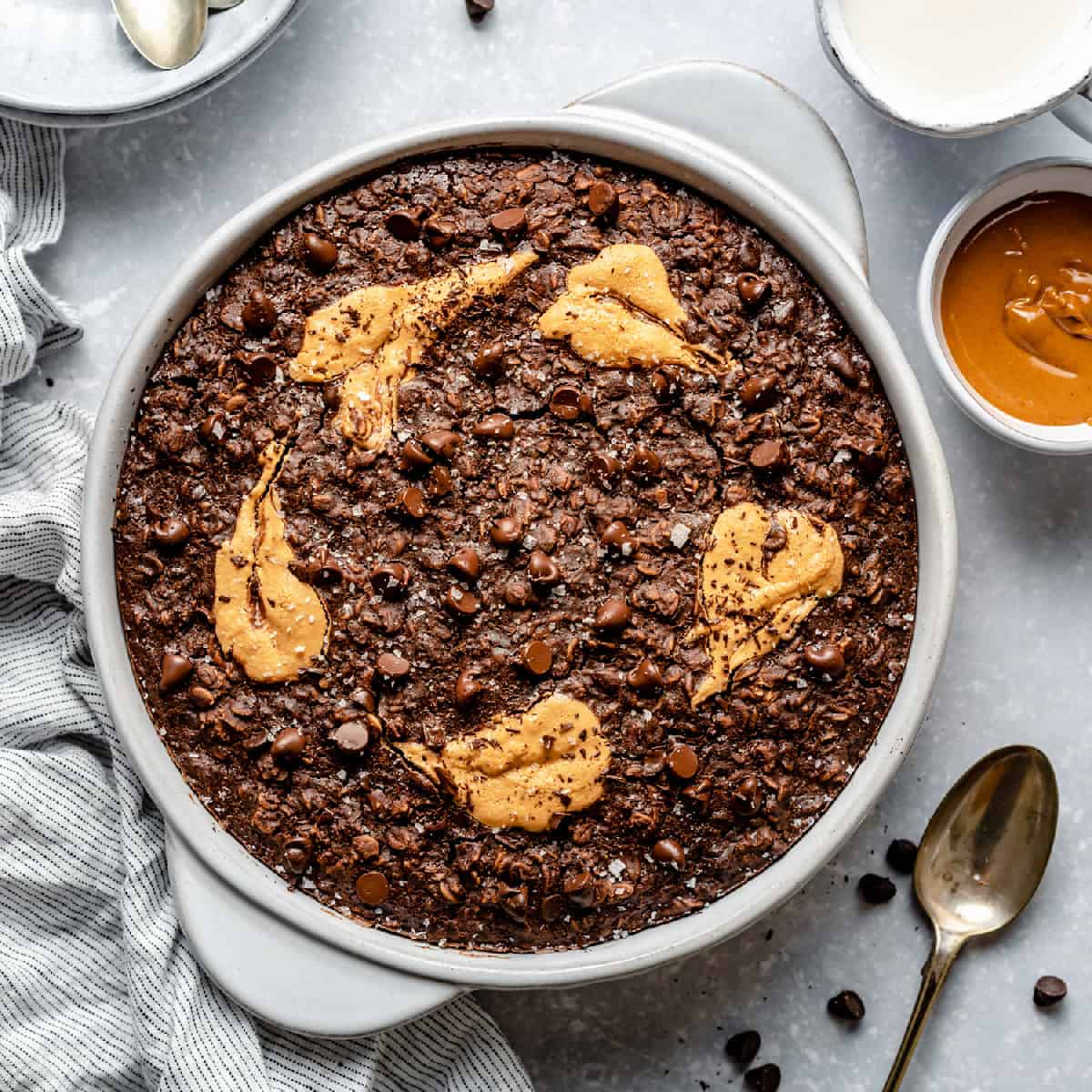 A baking dish with peanut butter baked oatmeal in it with peanut butter and bowls around.