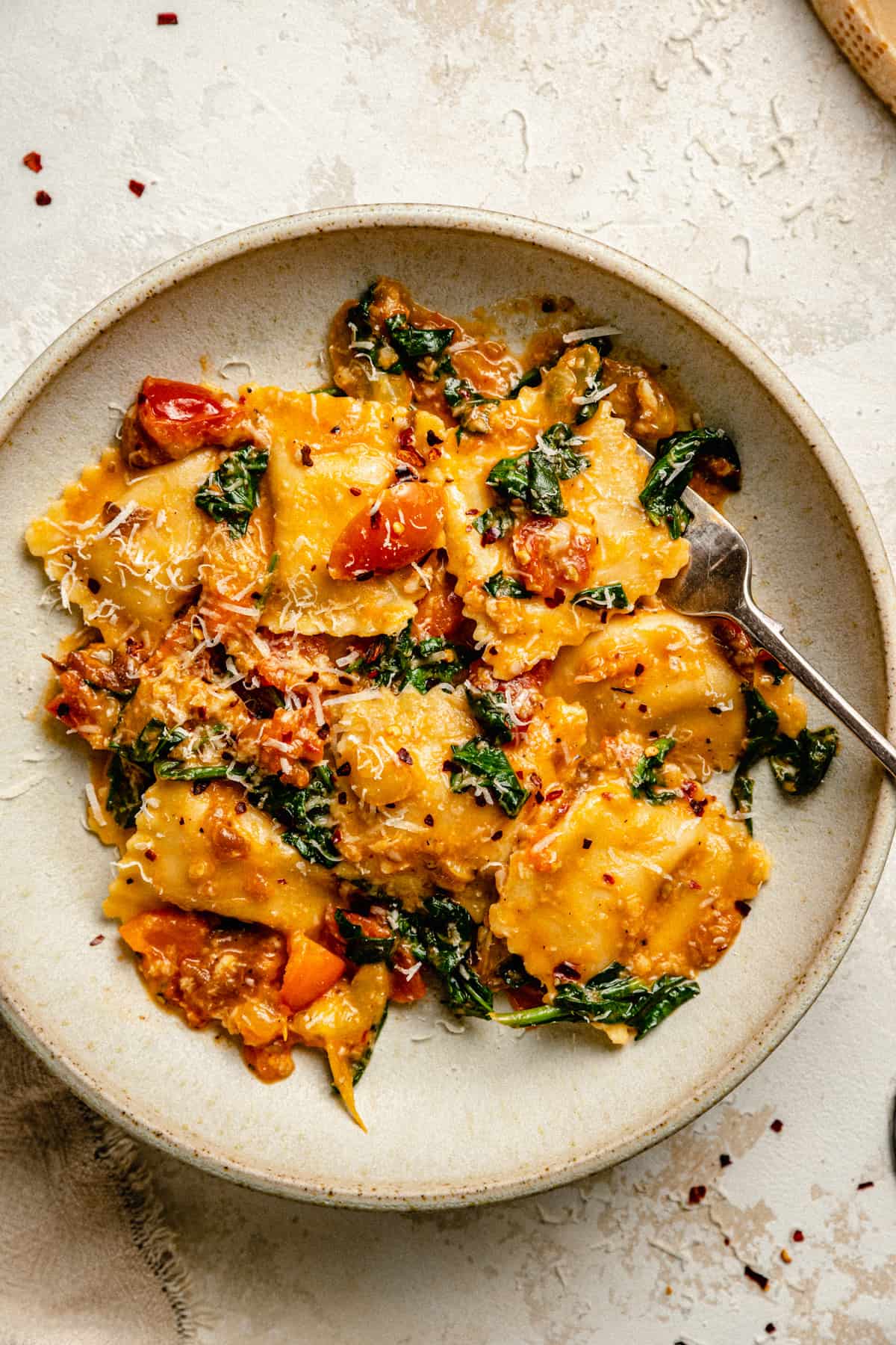 Tomato spinach pasta served in a cream bowl with a fork and parmesan wedge to the side.