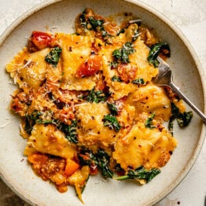 A close up of tomato spinach pasta in a cream bowl with a fork showing glossy pasta.