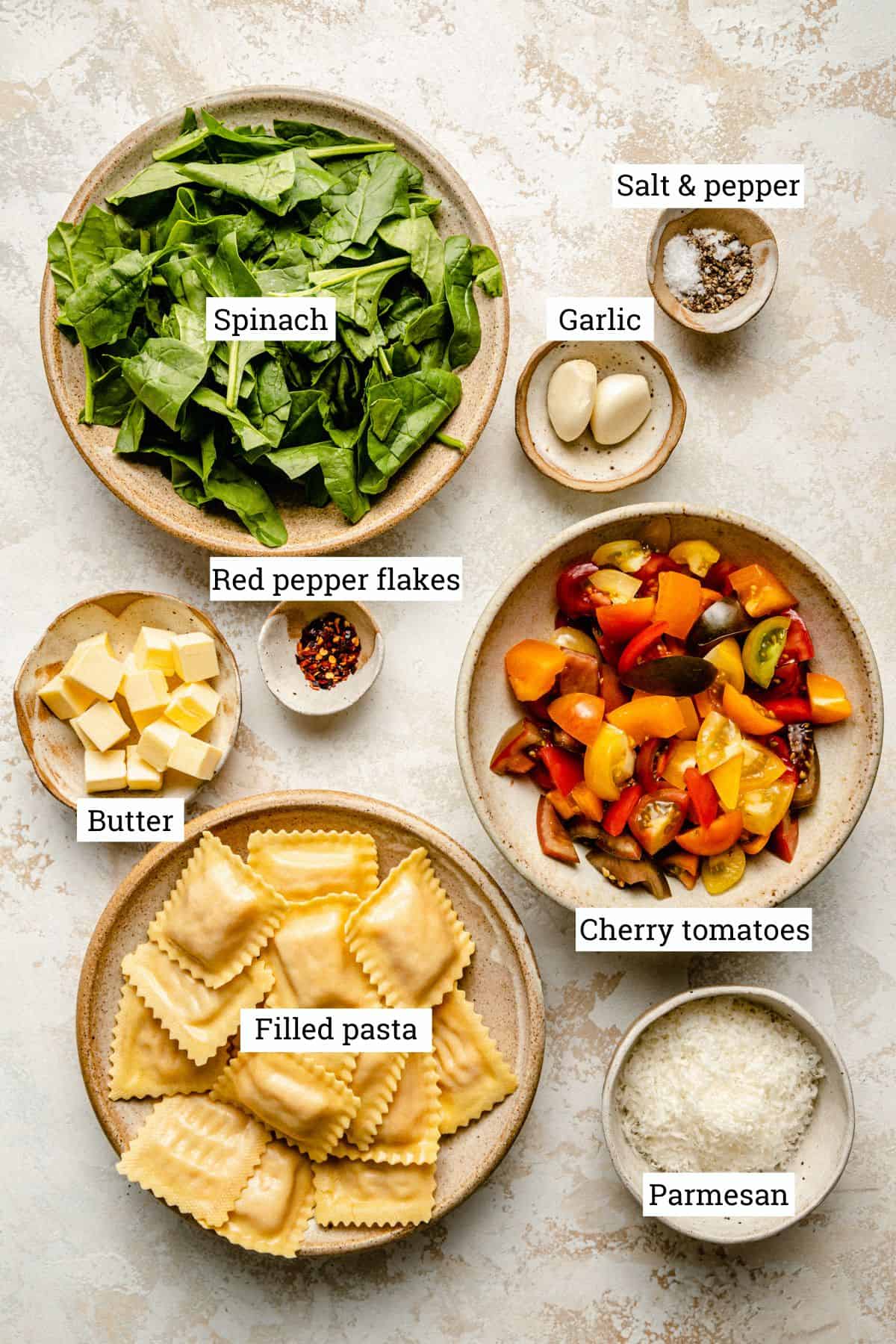 Ingredients for tomato spinach pasta in various bowls on a work surface.