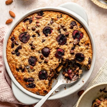 Chocolate chip baked oatmeal with cherries in a baking dish with a serving spoon scooping a serving out.