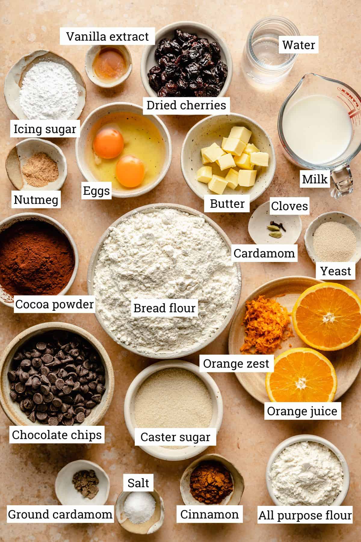 Ingredients for chocolate hot cross buns in various bowls on a surface with labels.