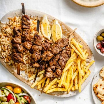 A table set with a white table cloth and a platter with fries rice and lamb souvlaki.