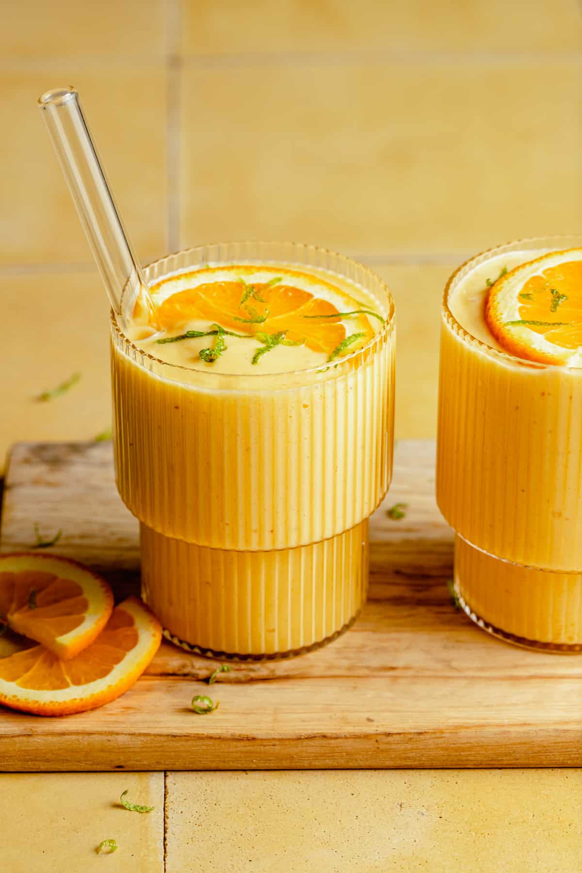 Two glasses of orange mango smoothie on a wooden board.