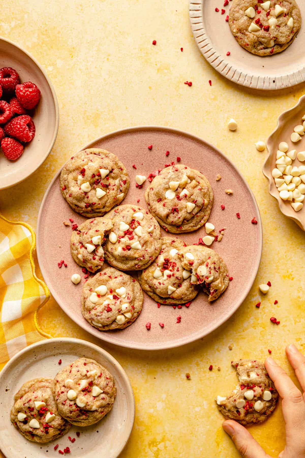 Several plates of various size with cookies on with a hand holding one with a bite taken.