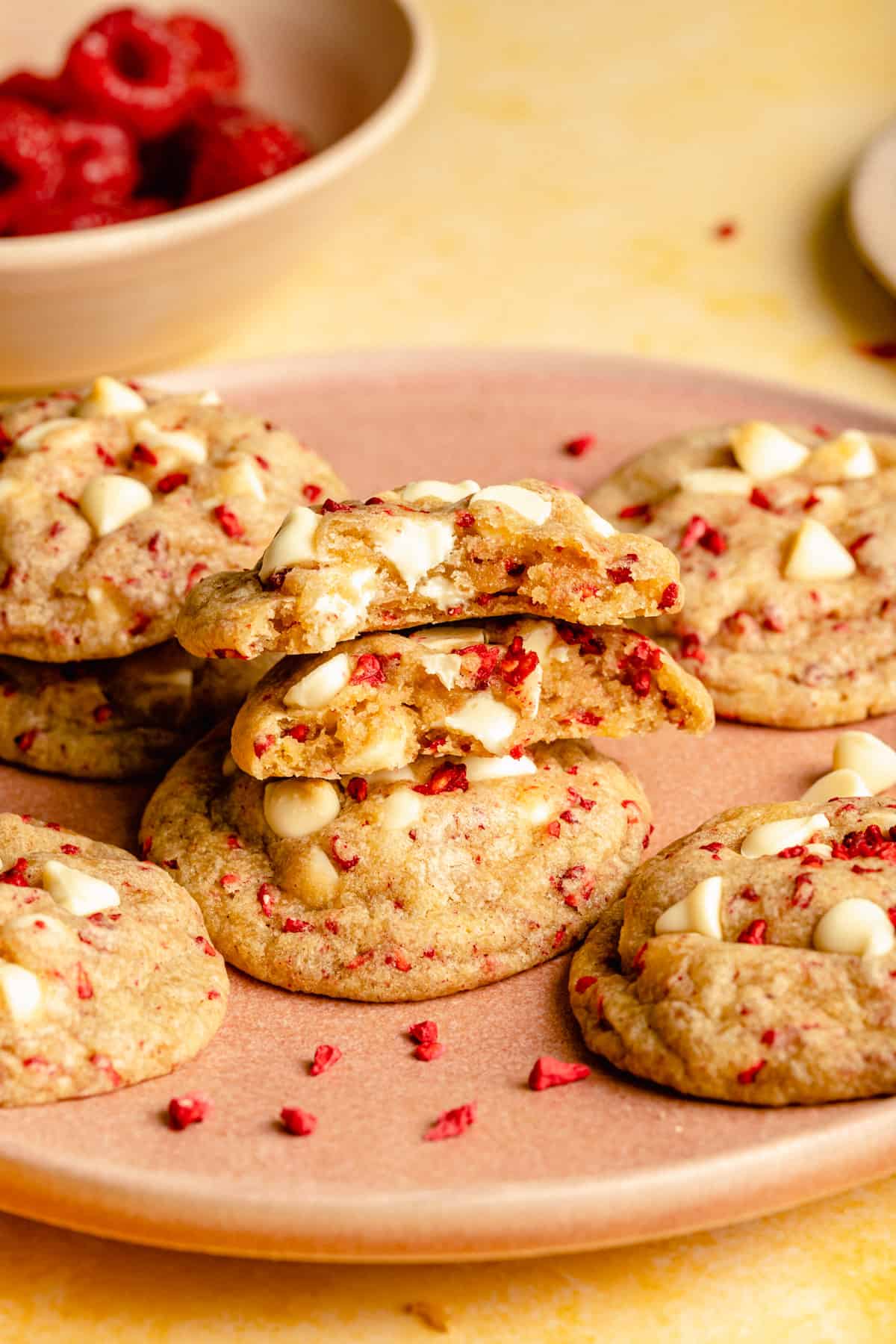 Close up of a cookie on a plate with a bite taken out of it with raspberries in the background.