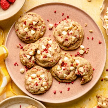 A plate of white chocolate raspberry cookies with chocolate chips and freeze dried raspberries around.