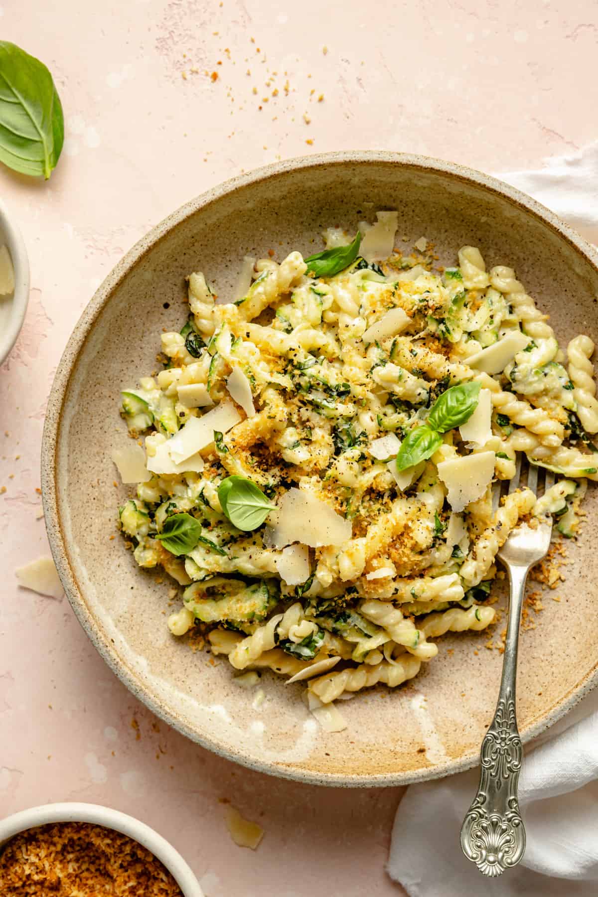 Lemon zucchini pasta in a bowl with a fork topped with shaved parmesan.