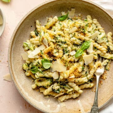 Lemon zucchini pasta in a bowl with breadcrumbs and shaved parmesan on top with a fork.