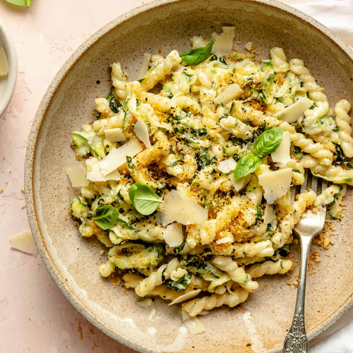 A bowl of creamy lemon zucchini pasta with parmesan and basil on the top with a fork. 