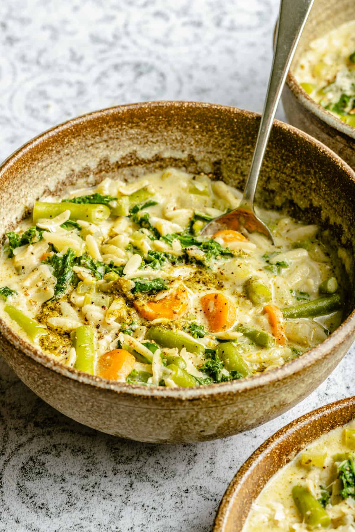 A bowl of vegetable orzo soup with a spoon and pesto on top.