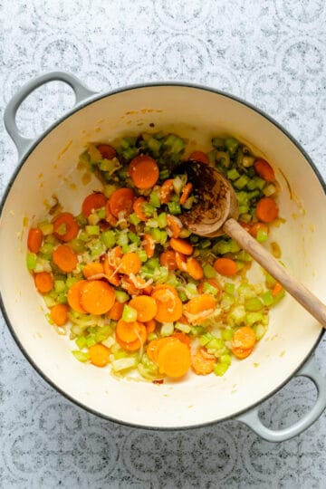 Sautéd carrot, celery and shallot in a cast iron dutch oven with a wooden spoon.