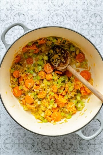 Toasting the orzo in the oil and vegetable mixture in a dutch oven with a spoon.