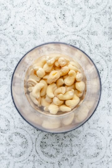 Soaked Cashews in water in a jug on a work surface.